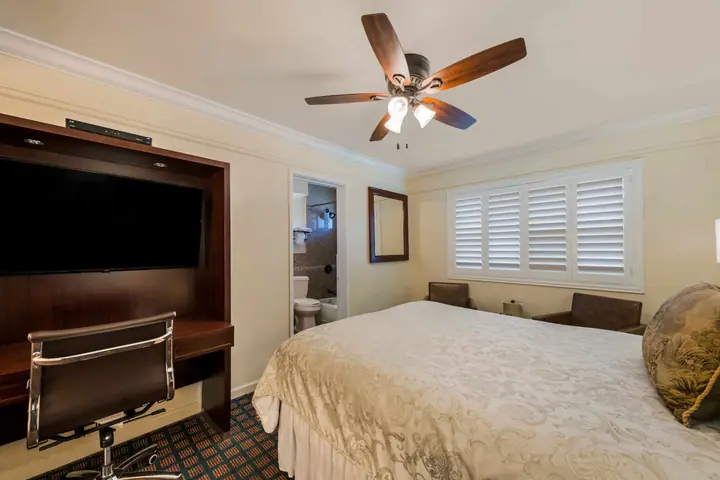 Queen bed facing a flat-screen TV and desk, with a doorway through to the bathroom
