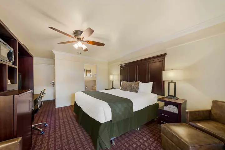 King bed with a dark wood headboard, a leather armchair with an ottoman and a work desk
