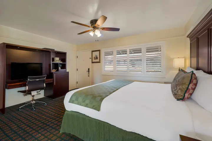 King bed facing a TV cabinet and work desk, beside a window with white shutters