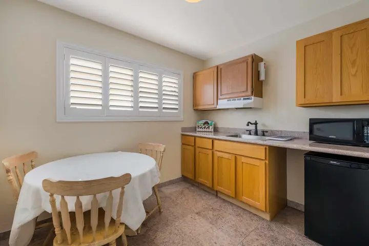 Kitchenette with wood cabinets, a sink, a microwave, a mini-fridge and a round dining table with two chairs