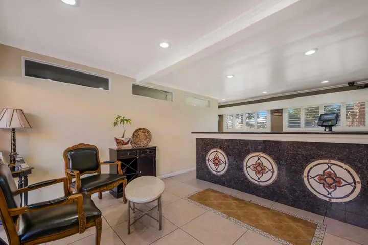 Lobby with a granite front desk inlaid with medallions, carved armchairs and a side table