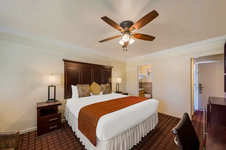 King bed with a rust runner, a ceiling fan and a doorway through to the bathroom