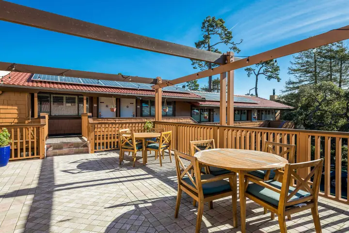 Sun deck with teak tables and chairs on a brick-paved terrace, a wooden railing and the inn's tiled roofs behind